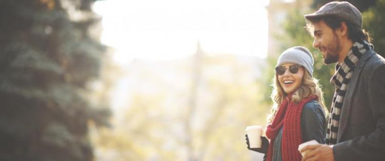 Photo of a couple walking in a park, drinking coffee from a coffee shop.