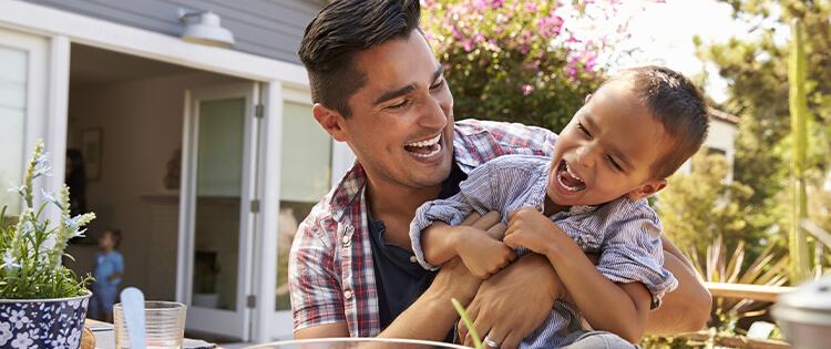 Un hombre riendo mientras sostiene a un niño que ríe.