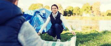 Photo of a woman opening a picnic blanket with a friend while at a campsite