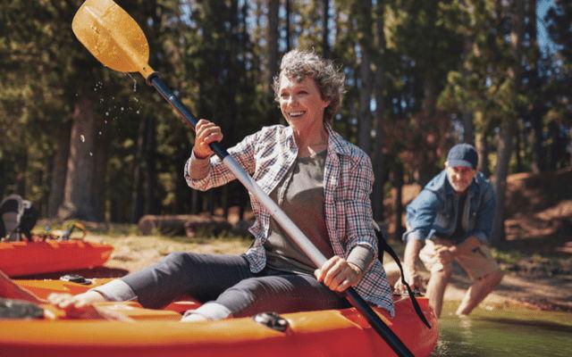 Photo of an older woman in a kayak getting pushed from shore by her husband.